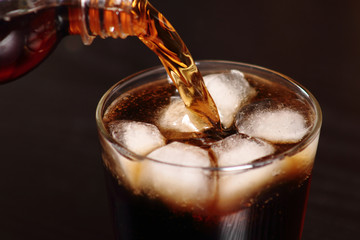 Pouring cola from plastic bottle into rocks glass with ice cubes at black background. Macro.