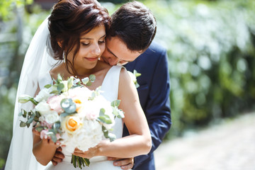 The bride and groom walk together in the park. Charming bride in a white dress, the groom is dressed in a dark elegant suit. Pretty bride and stylish groom. Wedding day. Marriage.