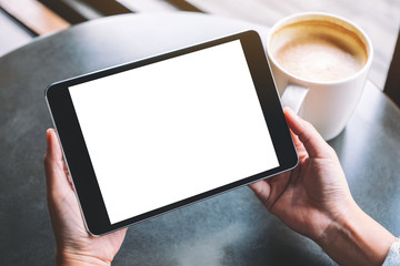Mockup image of a woman holding black tablet with white blank screen and coffee cup on the table