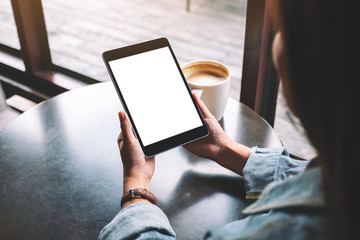 Mockup image of a woman holding black tablet with white blank screen and coffee cup on the table