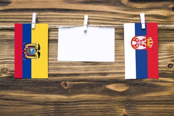 Hanging flags of Ecuador and Serbia attached to rope with clothes pins with copy space on white...