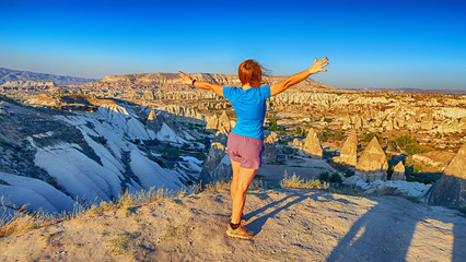 View from the back of a girl stands on a hill and looks at synset in Cappadocia, Turkey.