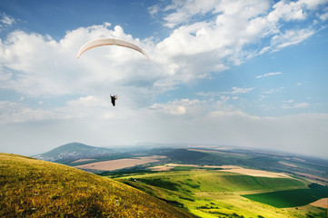 A paraglider flies in the sky in a cocoon suit on a paraglider over the Caucasian countryside with...