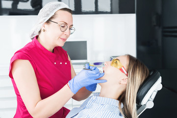 In the dentist's office. A female dentist in glasses is preparing to make a cast of the jaw of a young girl patient. Care clean mouth