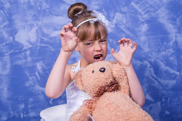 Beautiful little girl in a white dress and with a teddy bear on a blue background.