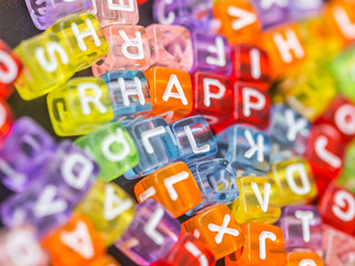 Closeup at happy word with many multicolored and colorful of alphabet plastic box on black board background. Happiness concepts and ideas.