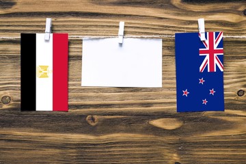 Hanging flags of Egypt and New Zealand attached to rope with clothes pins with copy space on white note paper on wooden background.Diplomatic relations between countries.