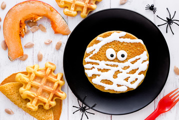 Mummy pancake , funny idea for kids for Halloween breakfast , pumpkin pancake with cream and candy eyes shaped mummy on black plate top view