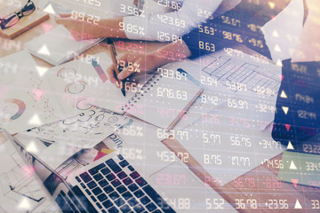 A woman hands writing information about stock market in notepad. Forex chart holograms in front....