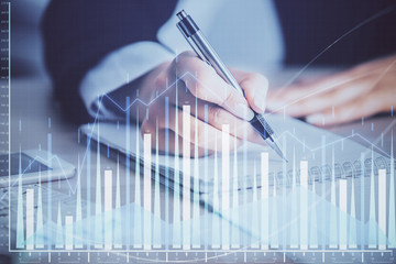 A woman hands writing information about stock market in notepad. Forex chart holograms in front....