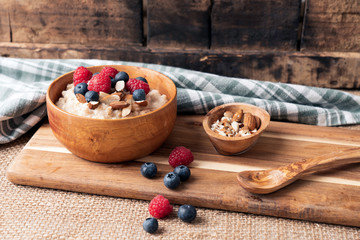 Oakmeal with whole wheat, almonds, raspberries and blueberries in wooden bowl on wooden rustic cuttingboard. Rustic backdrop. Food photography concept.