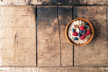 Wooden bowl of oakmeal with berries and almonds on top stand alone on wooden rustic background. Spacing for text to the left. Food photography and healthy living concept.