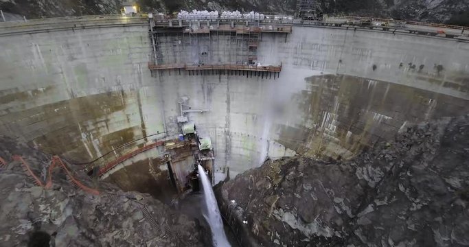 Drone shot water flow from hydro dam in mountains with black forest and winding road (Santa Anita Canyon, California, USA)