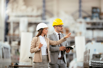 Businessman and businesswoman in factory. Man and woman in suits with helmets in factory discussing...