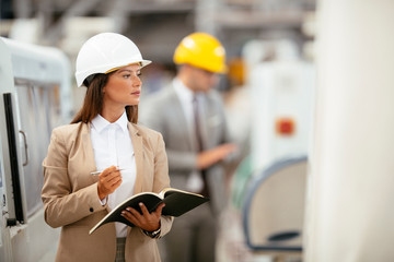 Portrait of businesswoman in factory. Young female architect with helmet in suit. 