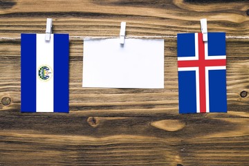 Hanging flags of El Salvador and Iceland attached to rope with clothes pins with copy space on white note paper on wooden background.Diplomatic relations between countries.