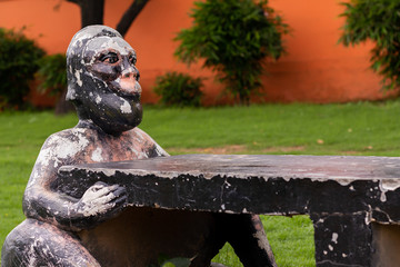 A rock bench with weathered monkey statues and red wall in the background