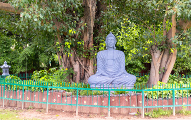 Wide shot of a Grey black buddha statue sitting under a tree. Meditation concept