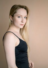 Fototapeta premium Graceful young woman in a black top posing against beige wall.