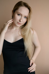 Graceful young woman in a black top posing against beige wall.