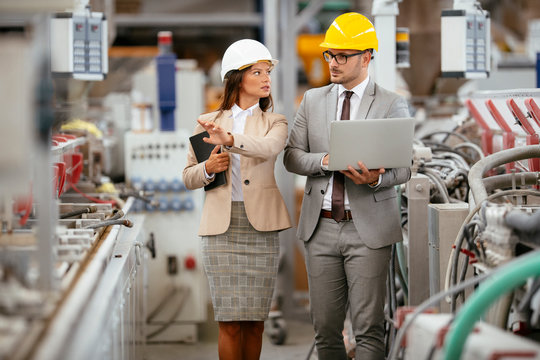 Businessman and businesswoman in factory. Man and woman in suits with helmets in factory discussing work.