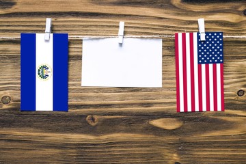 Hanging flags of El Salvador and United States attached to rope with clothes pins with copy space on white note paper on wooden background.Diplomatic relations between countries.