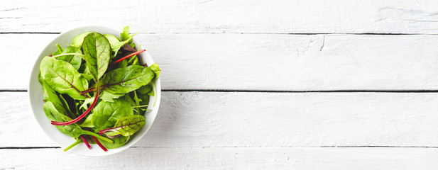 Overhead shot of fresh green salad with spinach, arugula and beetroot leaves in bowl on white...