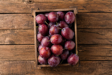 Juicy plums in box on rustic wooden table. Top view