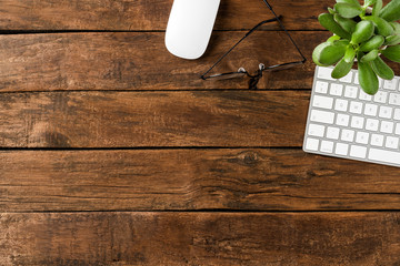 Modern computer keyboard with mouse, eyeglasses and small flower on wooden background. Office desktop