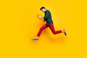 Fototapeta na wymiar Full size profile side photo of positive cheerful brunet hair use his cellphone search find discounts jump run feel content wear green shirt red pants trousers isolated over yellow color background