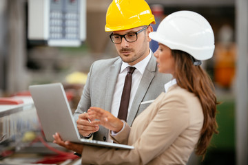 Businessman and businesswoman in factory. Man and woman in suits with helmets in factory discussing work.