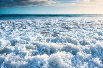 Seascape with surf waves, bright sky and white clouds