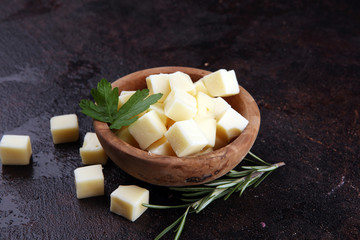 cheese cubes in wooden bowl with parsley. cheese pieces on table