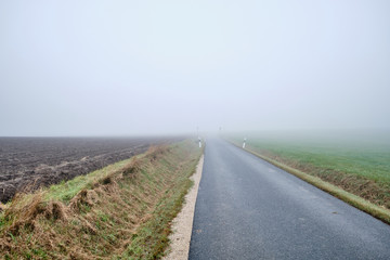 Countryside road to nowhere -  narow street with diminishing perspektive leading into the fog. Seen in Germany near Oedenberg, Bavaria in October.