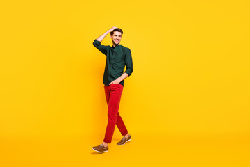 Fototapeta premium Full length body size turned photo of cheerful youngster stepping away from where he is looking wearing shoes adjusting his hair isolated over vivid color background