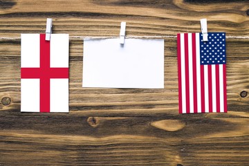 Hanging flags of England and United States attached to rope with clothes pins with copy space on white note paper on wooden background.Diplomatic relations between countries.