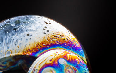 close up of a colorful soap bubble isolated on a black background, looking like a planet in space.