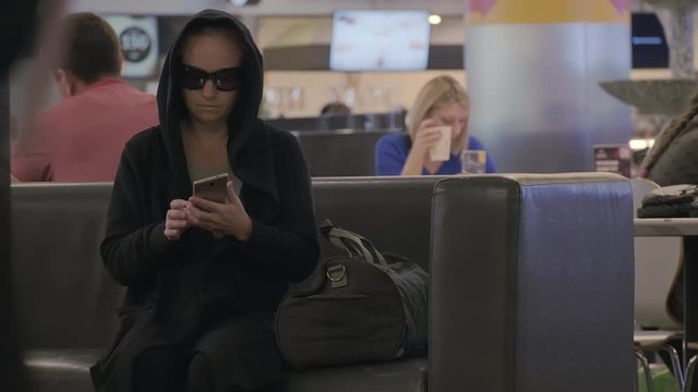 terrorist leaves bag with bomb on sofa in shopping center at crowded place. woman in black glasses and hood starts countdown timer and puts it in bag with explosives.