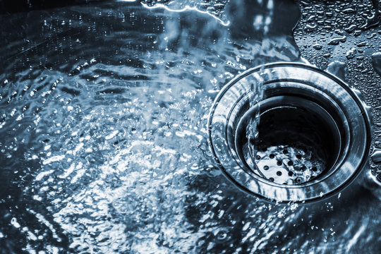 stream of clean water pouring into a steel sink in the kitchen. Toned image