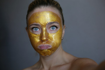 Portrait of young woman posing with golden face mask. Skin acne treatment. Golden face mask. 