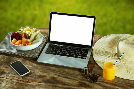 Blank screens of laptop and smartphone on a wooden table outdoors with nature on background, mock up. Fruits and fresh juice near by. Concept of creative workplace, business, freelance. Copyspace.