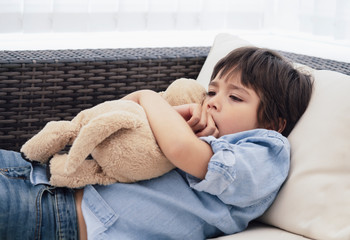 Dramatic portrait of little boy lying on sofa and cuddling dog toy with scared face,Unhappy Child sitting alone and looking out with worrying face,Toddler boy on corner punishment sitting