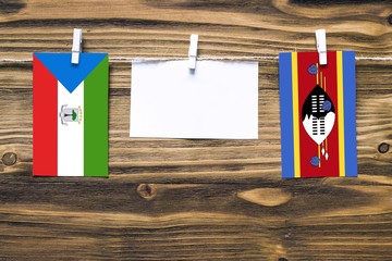 Hanging flags of Equatorial Guinea and Swaziland attached to rope with clothes pins with copy space on white note paper on wooden background.Diplomatic relations between countries.