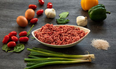 Minced beef on a white plate.  The leaves of spinach, red and yellow tomatoes, garlic  and onions. Close up photo