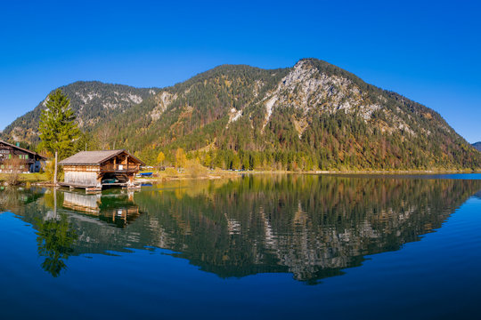 wooden boathouse next scotch pine at wonderful reflecting lake plansee in autumn
