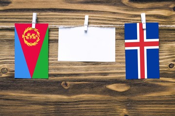 Hanging flags of Eritrea and Iceland attached to rope with clothes pins with copy space on white note paper on wooden background.Diplomatic relations between countries.