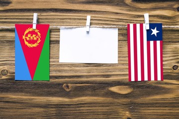 Hanging flags of Eritrea and Liberia attached to rope with clothes pins with copy space on white note paper on wooden background.Diplomatic relations between countries.