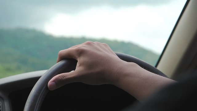 Hand on right steering wheel driving in the middle of a valley with dramatic sky