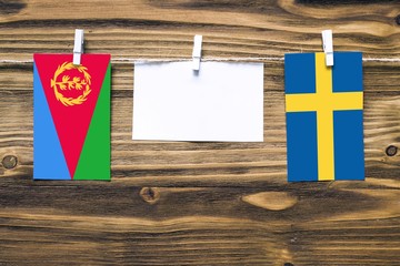 Hanging flags of Eritrea and Sweden attached to rope with clothes pins with copy space on white note paper on wooden background.Diplomatic relations between countries.