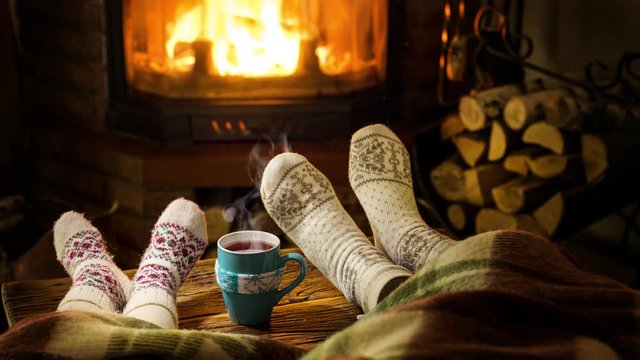 Warm atmosphere near the fireplace. Female and children's feet in woolen socks, steam rises from a hot drink.